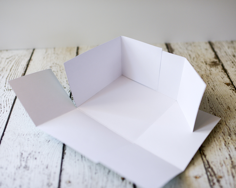 A partially assembled cardstock box lid with two corners clipped using small binder clips while glue dries