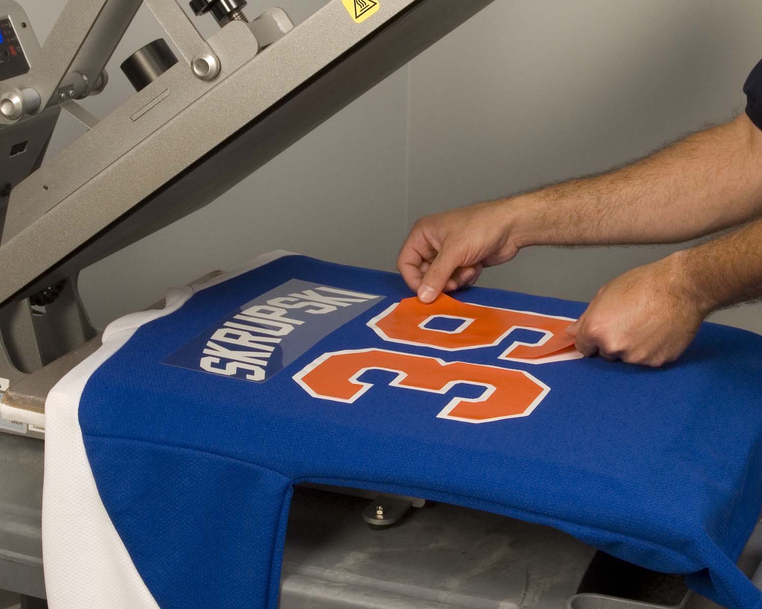 A red polyester sports jersey laid flat on a heat press platen with a white heat transfer vinyl design positioned on the chest area before pressing