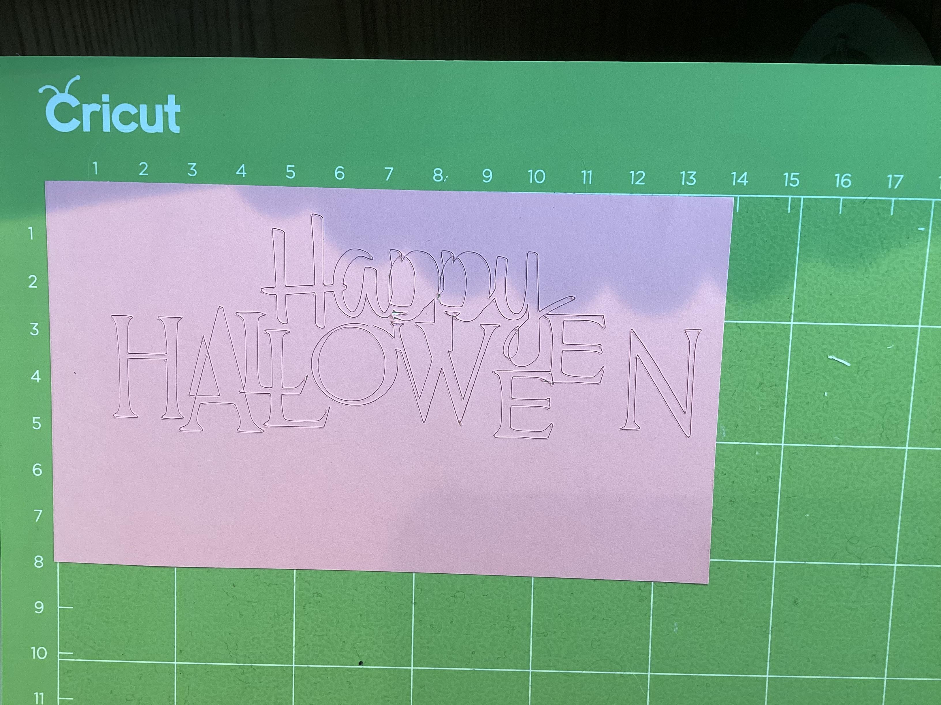 A sheet of paper on a Cricut mat showing two sets of tiny cut marks that are slightly misaligned, indicating a tracking shift