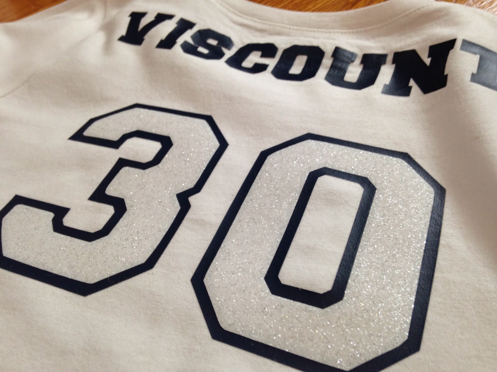 A white HTV name on a red polyester jersey showing a noticeable pink tint developing in the vinyl after pressing