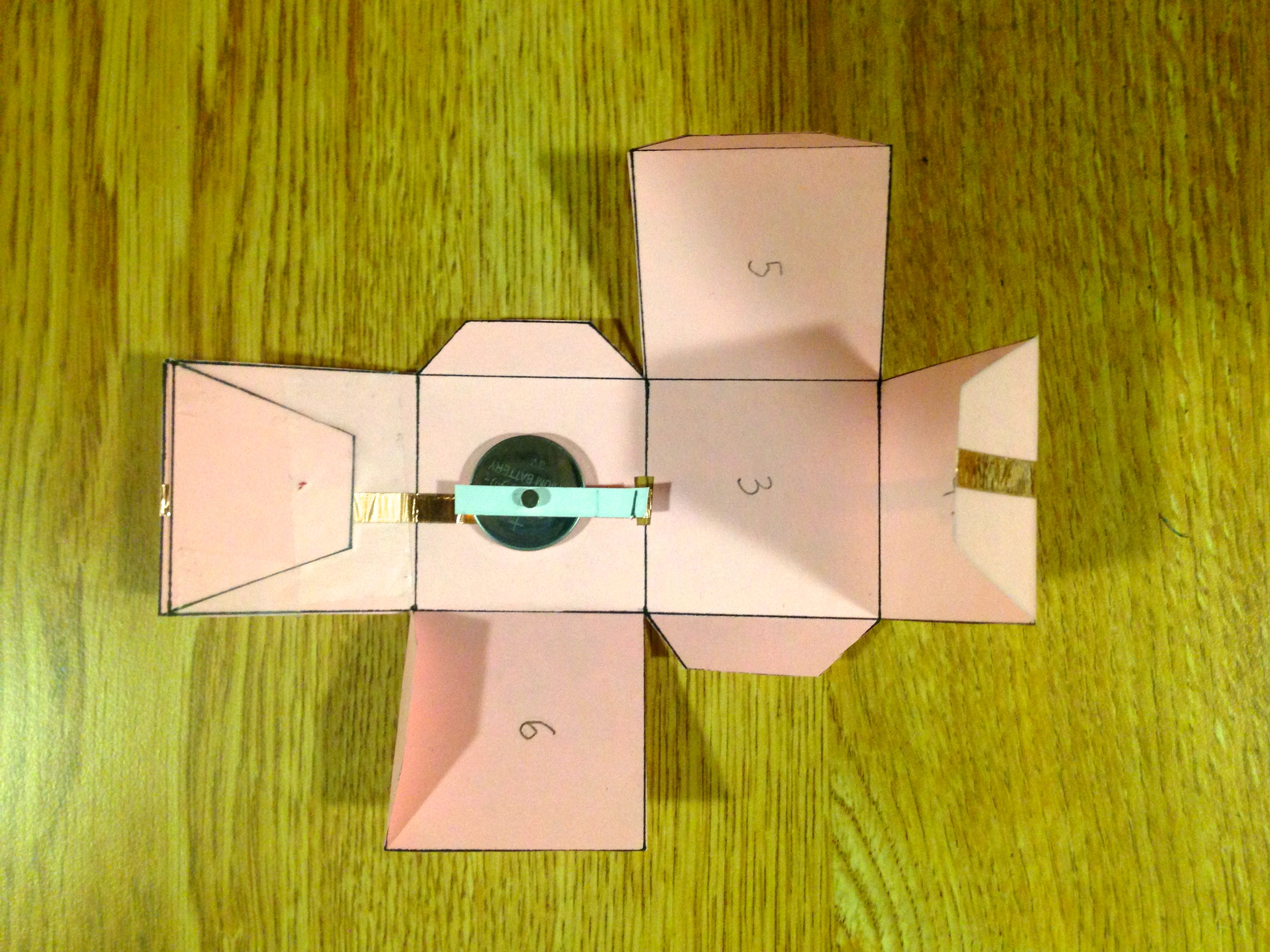 Hands folding scored cardstock into a box shape on a craft table with a bone folder nearby